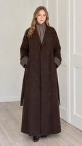 Front full view of woman wearing brown double-breasted maxi longline coat with plaid cuffs