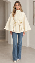 Front view of cream high neck belted cape coat paired with jeans
