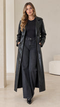 Front full-length view of model wearing a black faux leather maxi trench coat open over black top and dark jeans