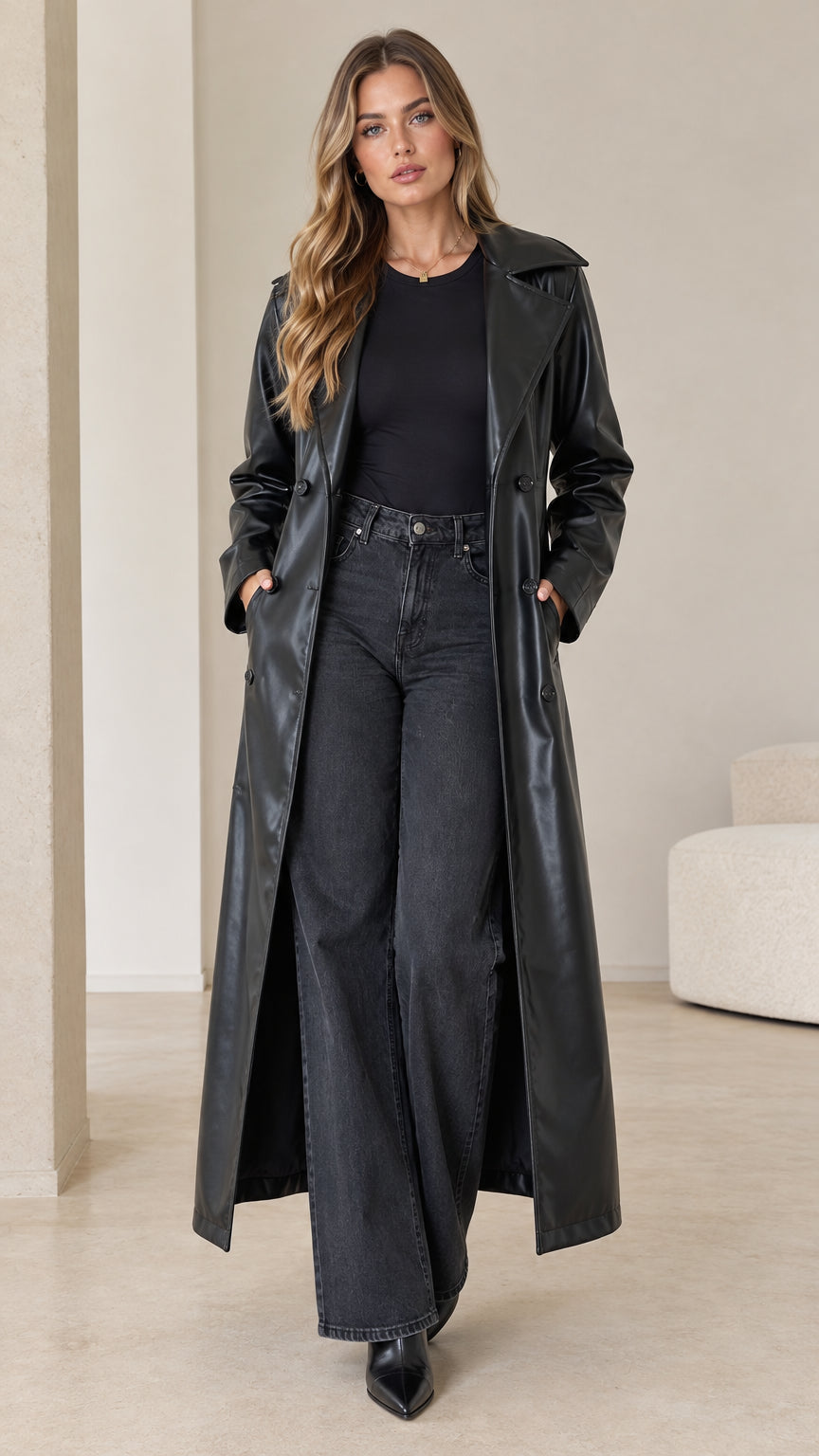 Front full-length view of model wearing a black faux leather maxi trench coat open over black top and dark jeans