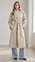 Front full view of woman wearing beige high-neck belted trench coat with denim trousers