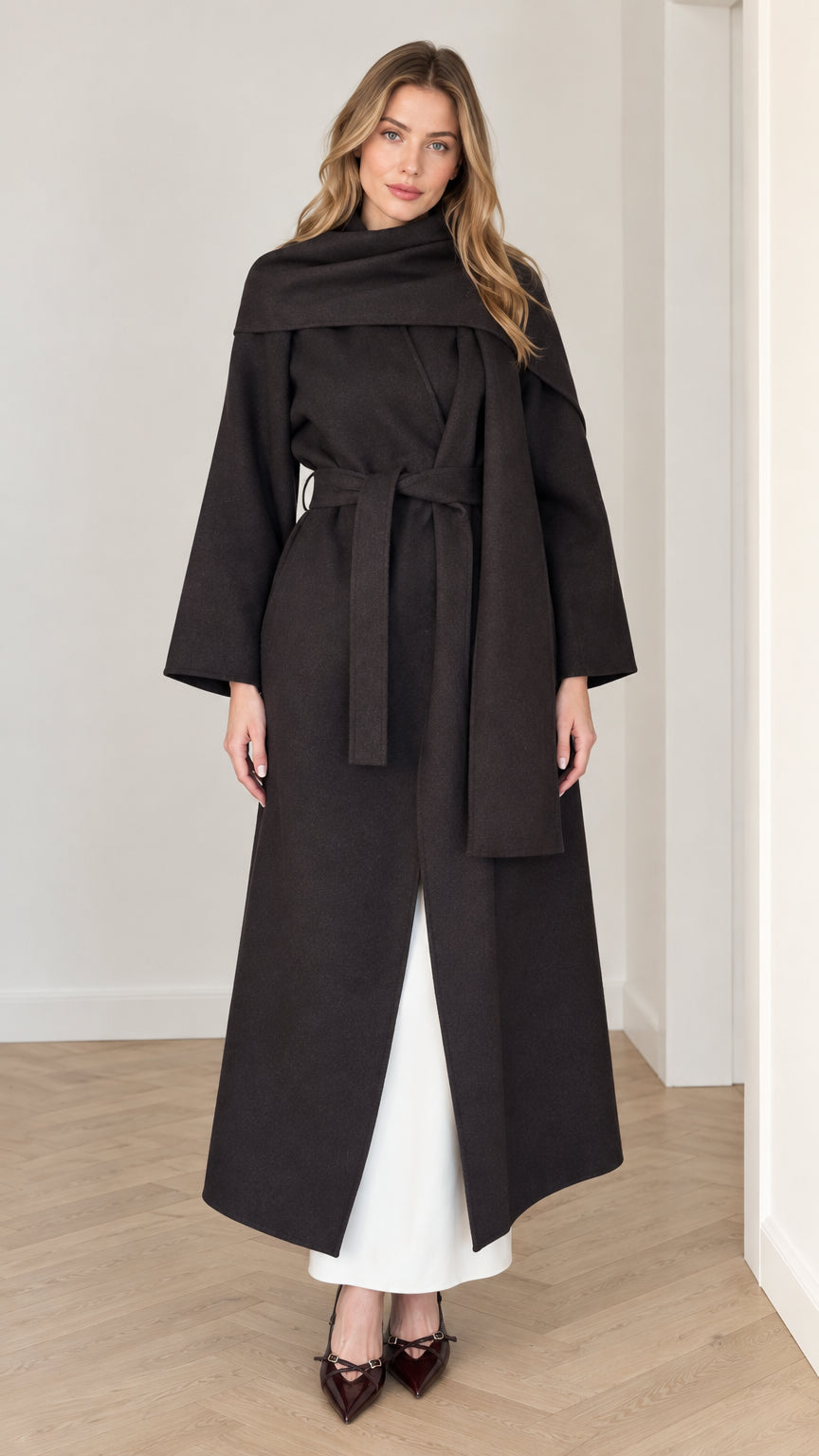 Model wearing long black maxi wrap coat with integrated drape scarf collar and tie belt, front view