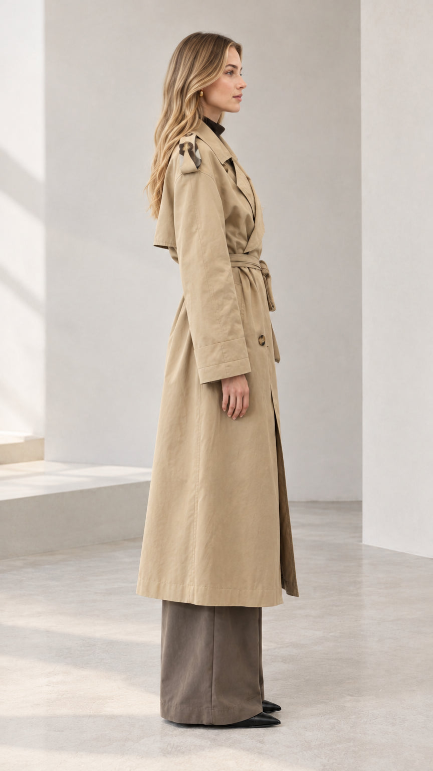 Side profile view of woman wearing long khaki belted trench coat