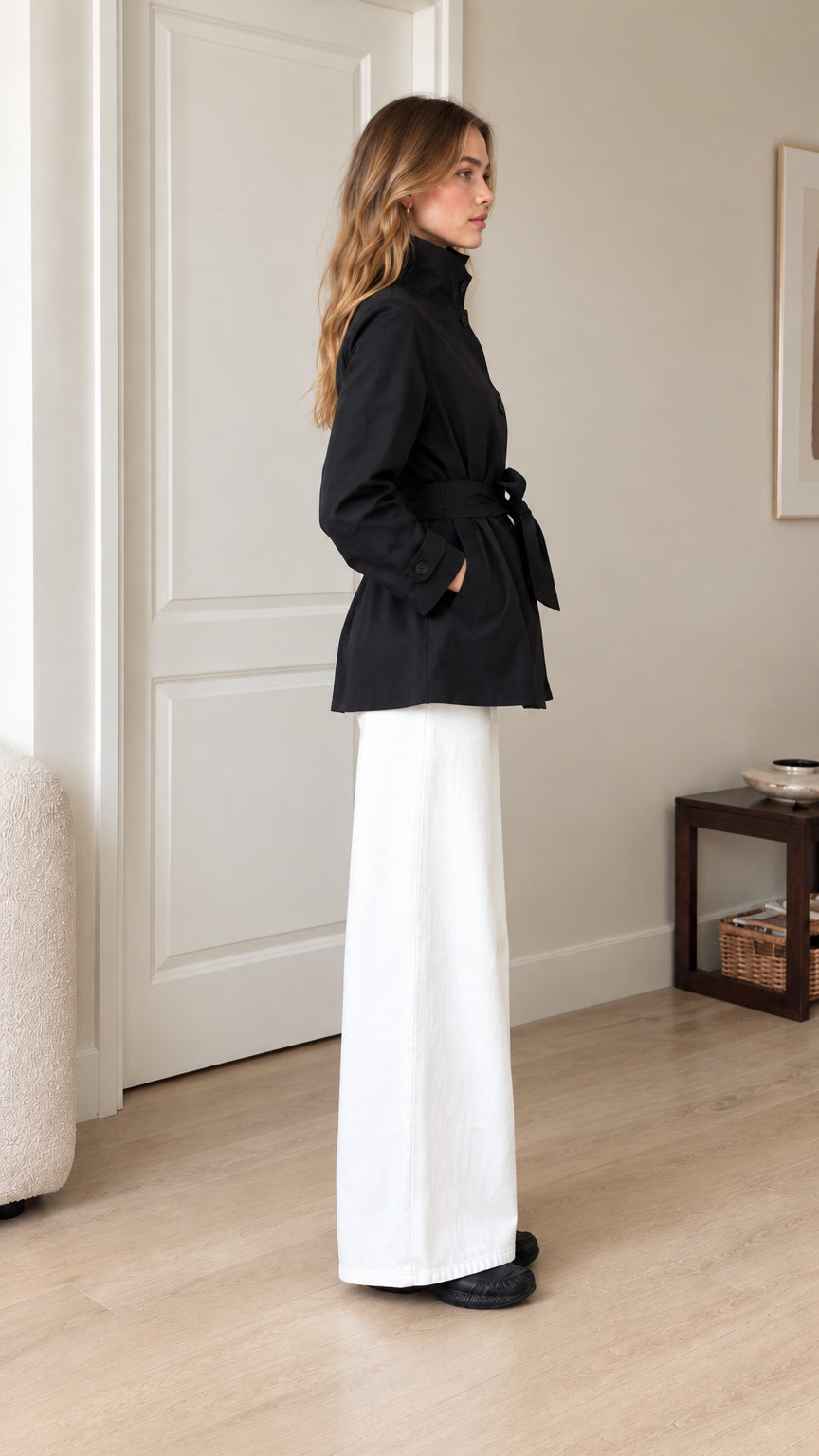 Side profile view of model wearing black short belted trench jacket