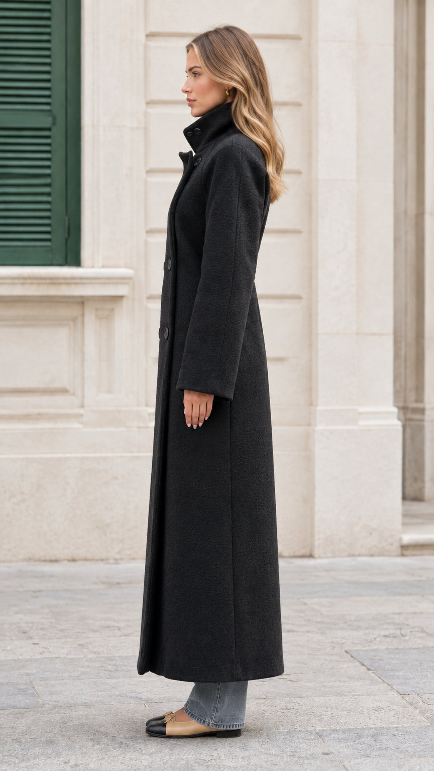 Side profile view of the black full-length double-breasted overcoat on model