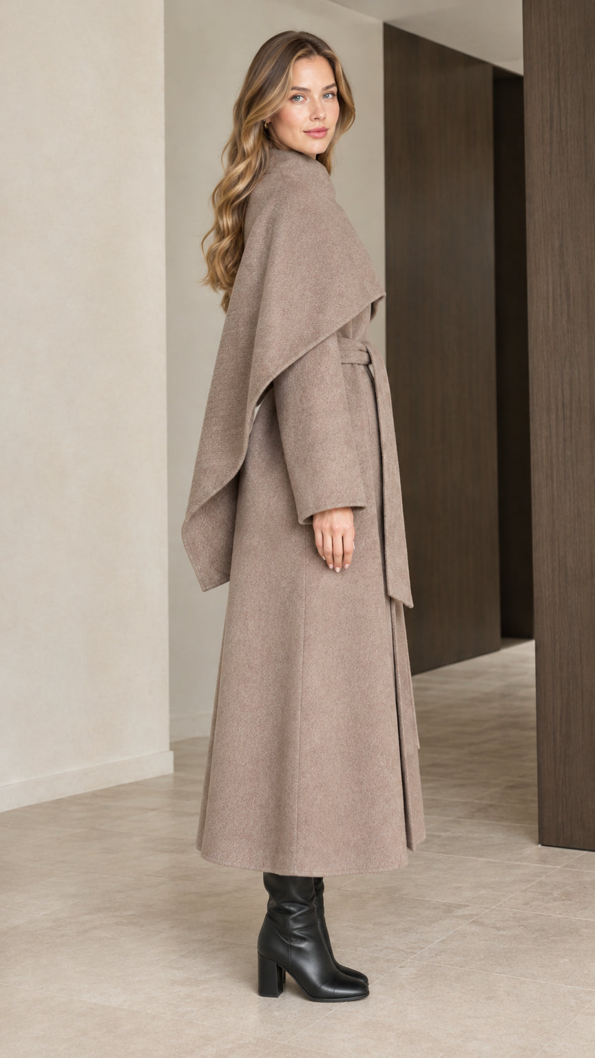 Side profile view of woman modeling taupe long overcoat with layered shoulder cape