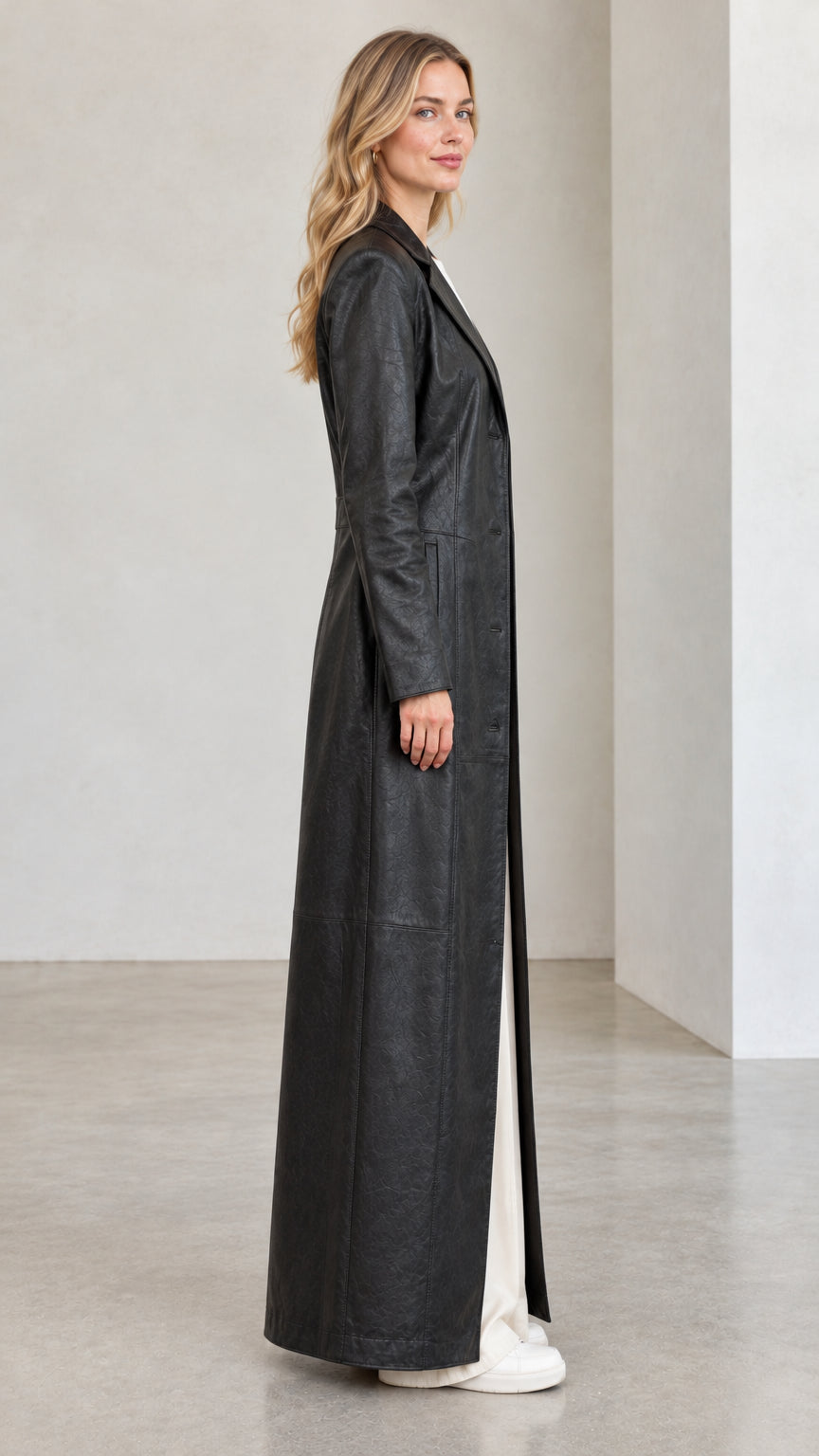 Side profile view of woman wearing full-length black faux leather trench coat