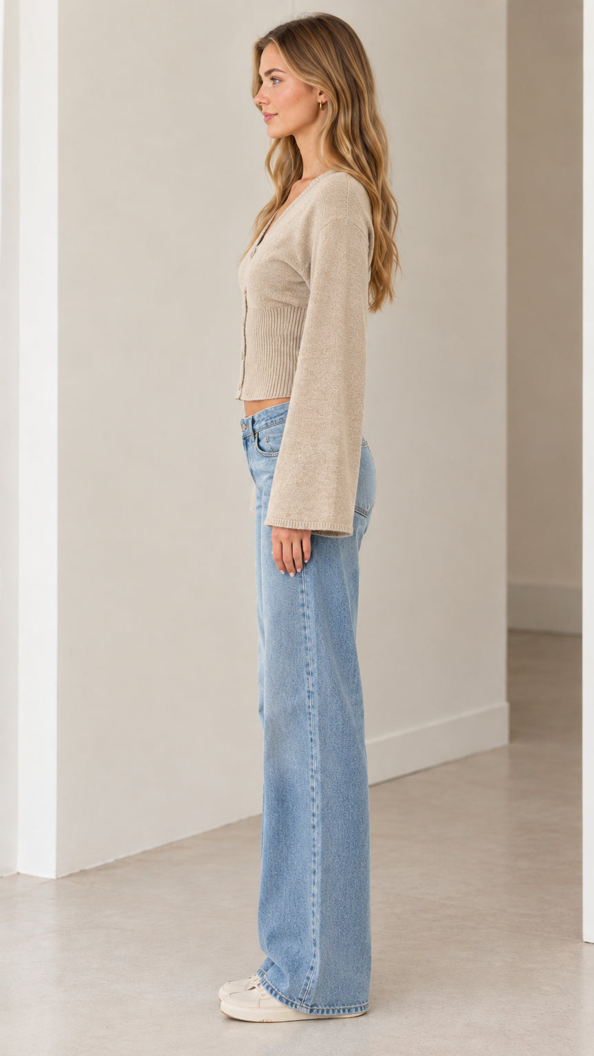 Side profile view of beige bell sleeve knit cardigan sweater paired with light denim