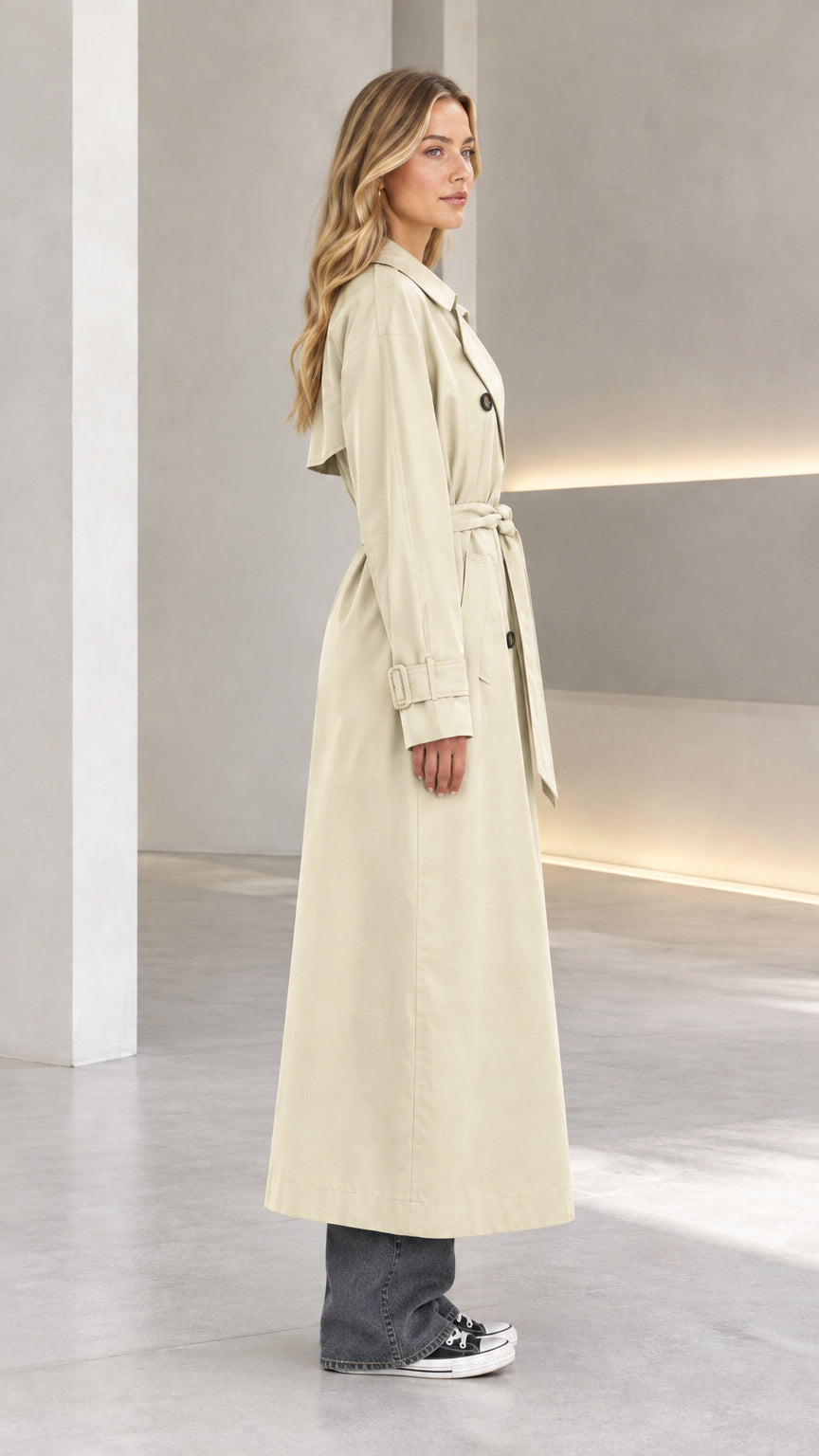 Side profile view of beige long trench coat showing relaxed fit and clean drape