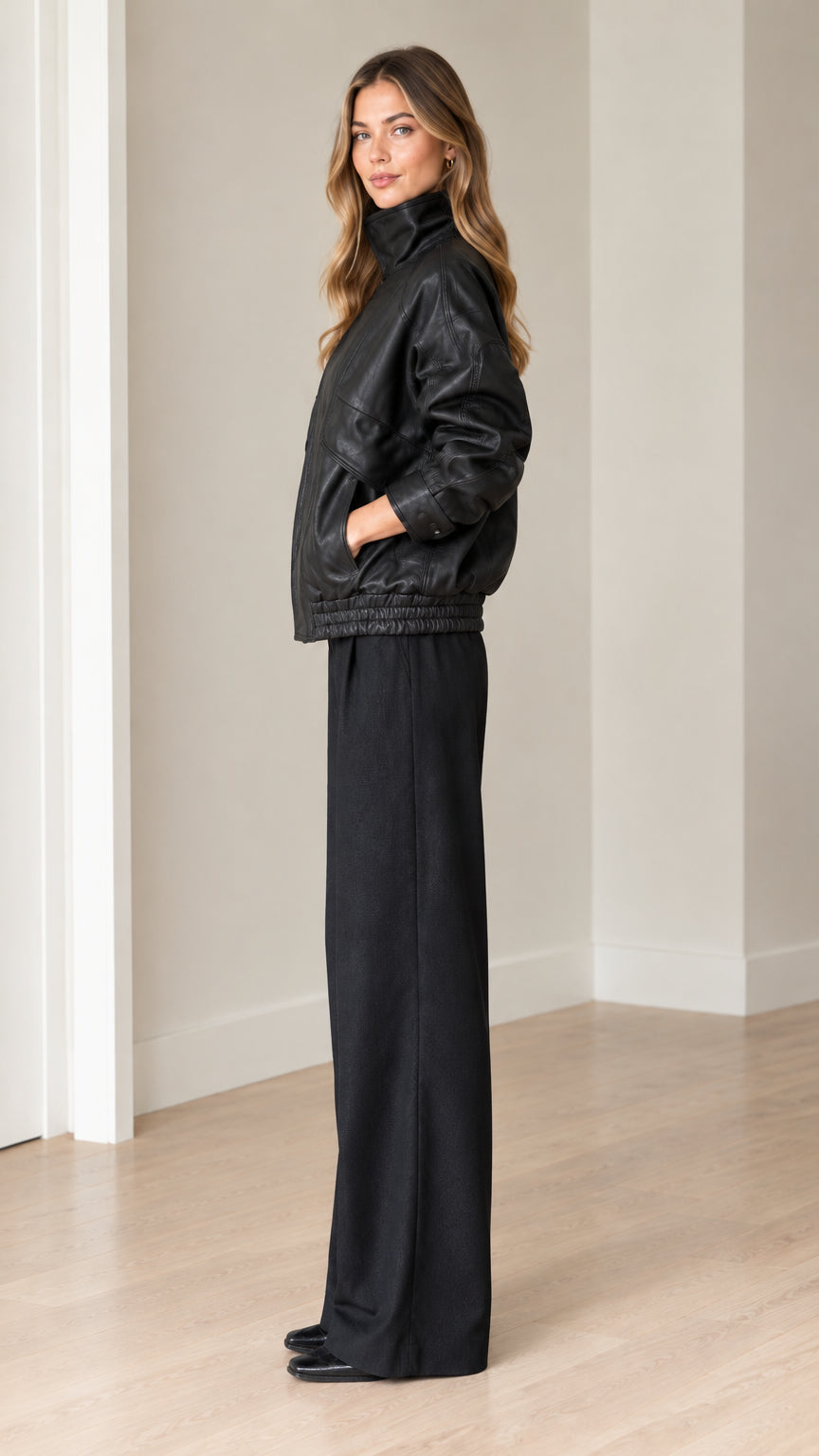 Side profile of model wearing black faux leather jacket and wide-leg trousers