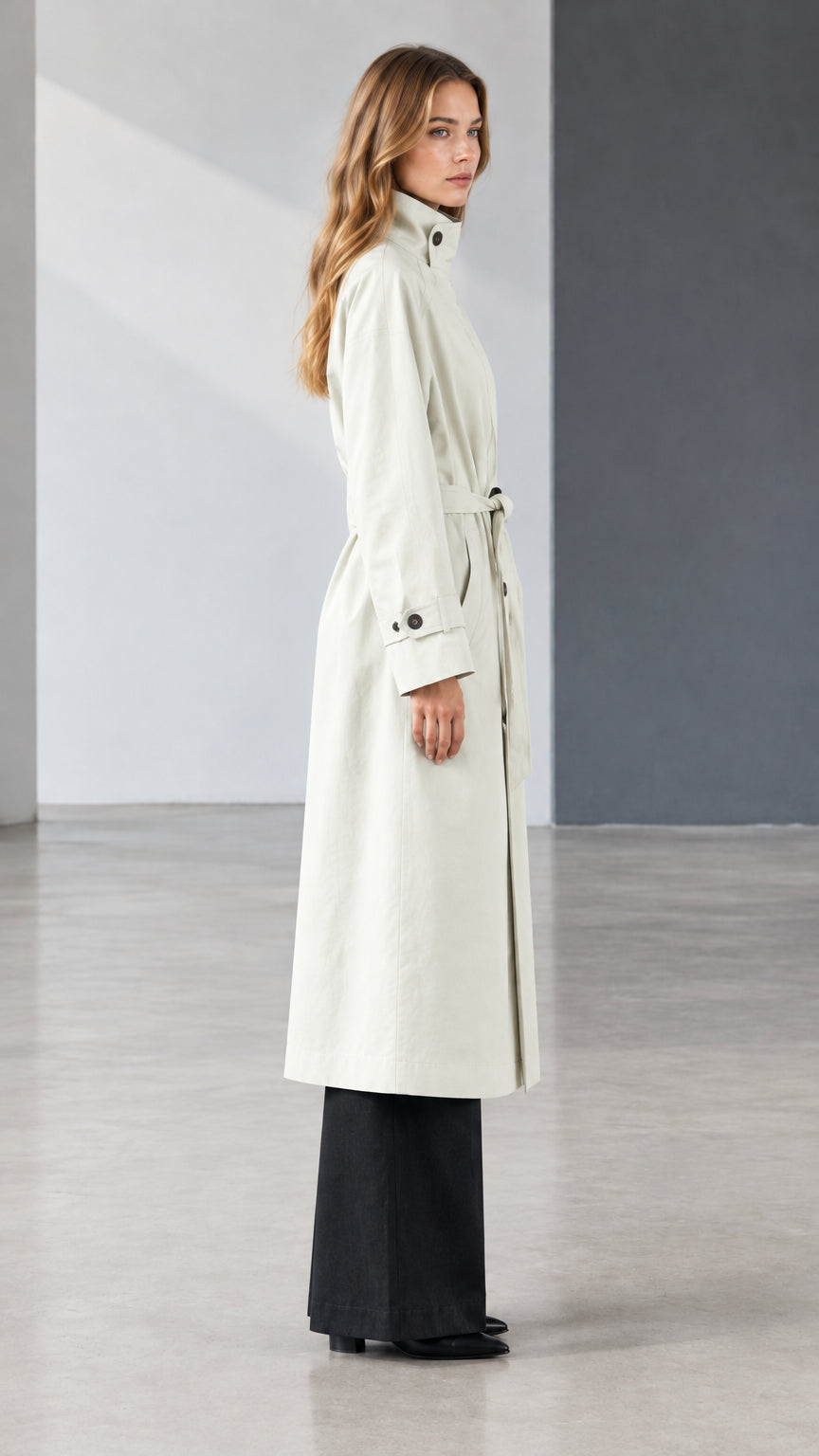 Side profile view of model wearing off white longline trench coat with self tie belt