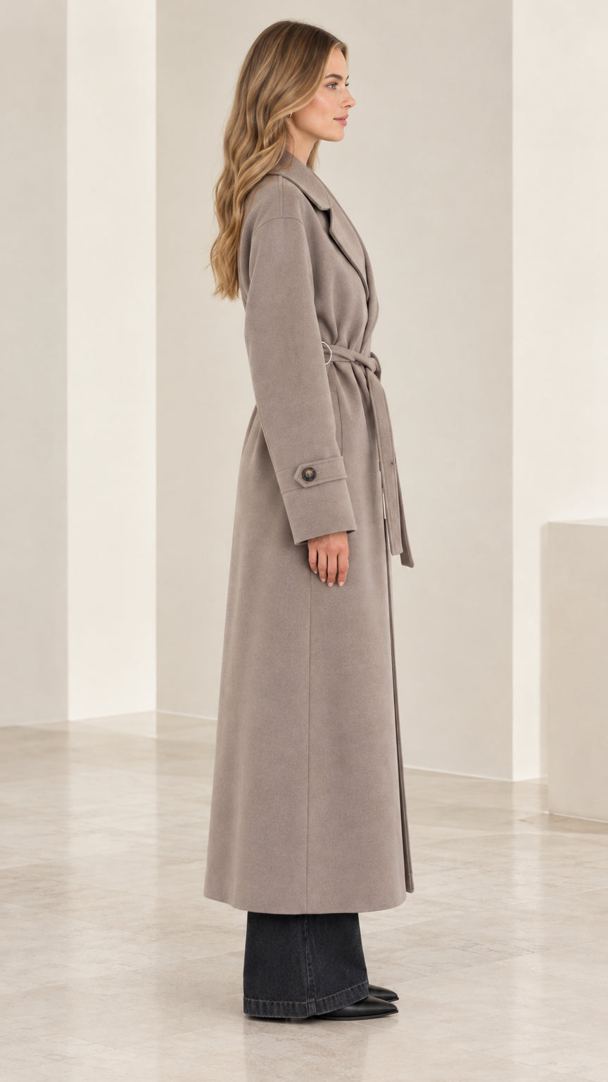 Side profile view of woman wearing a full-length taupe belted trench coat