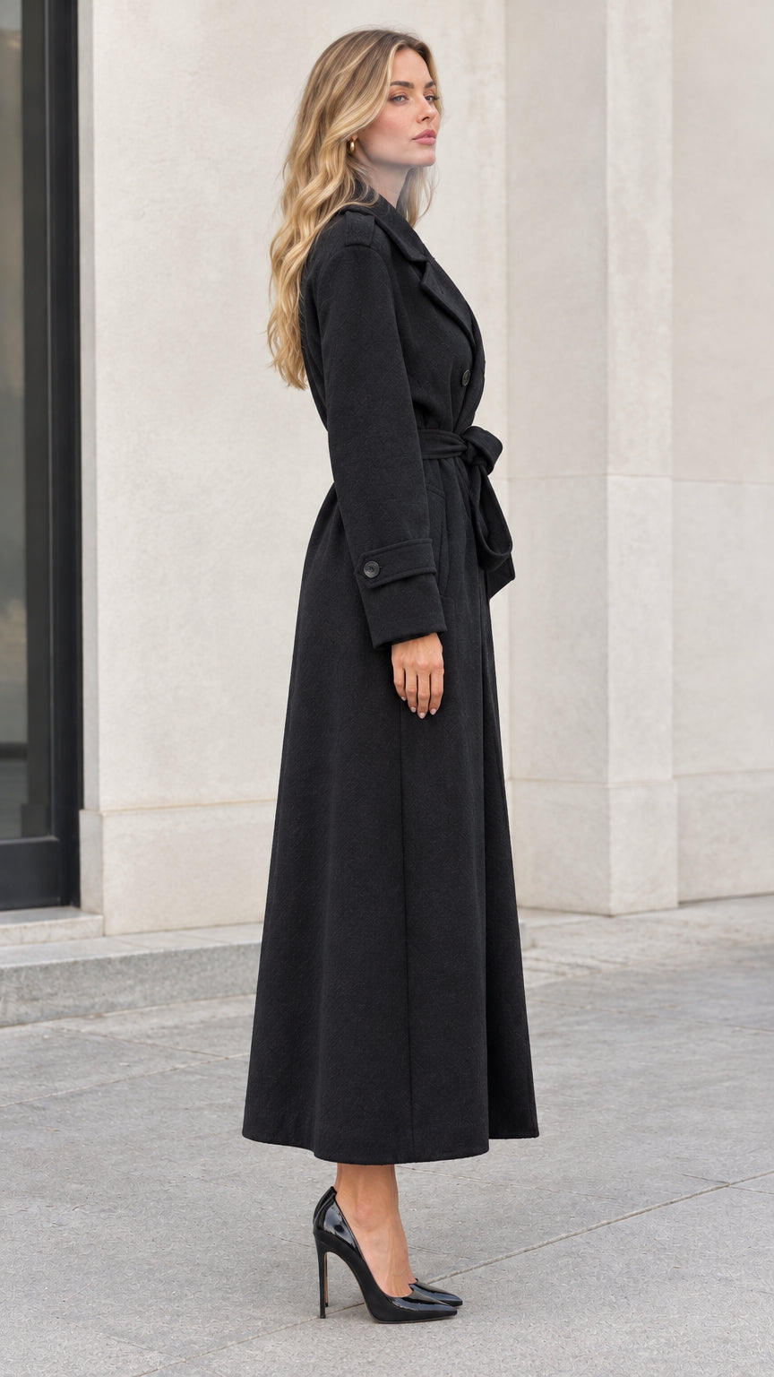 Side profile view of woman wearing black long belted trench coat with heels