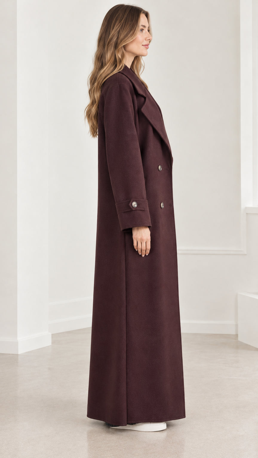 Side profile of model wearing a floor-length burgundy overcoat