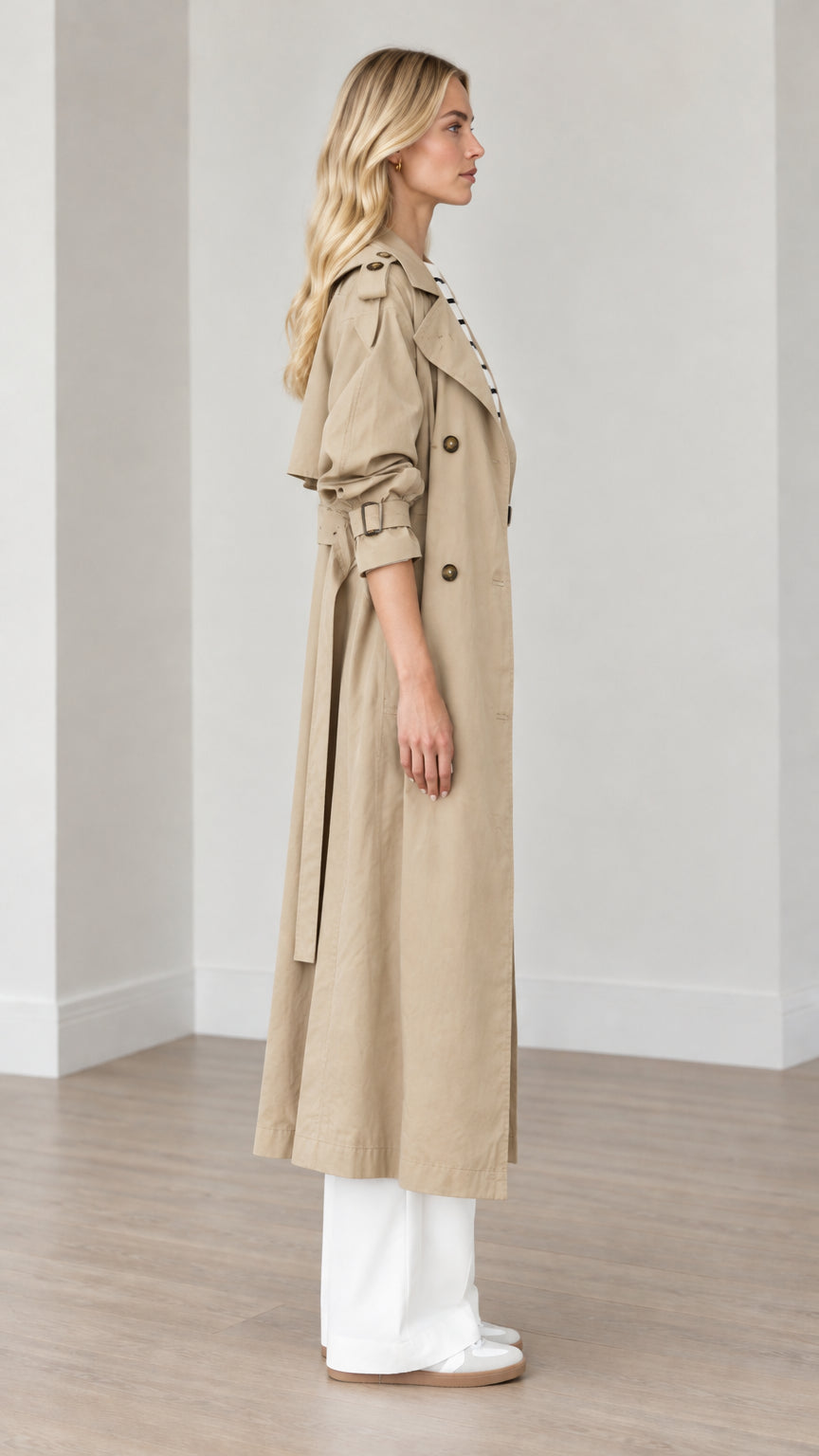 Side profile view of woman wearing khaki belted long trench coat with wide-leg trousers