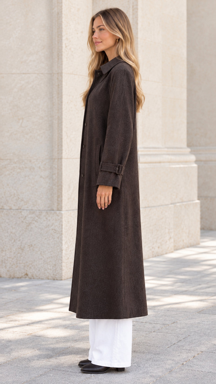 Side profile view of dark brown maxi coat showcasing longline silhouette and buckled cuff detail