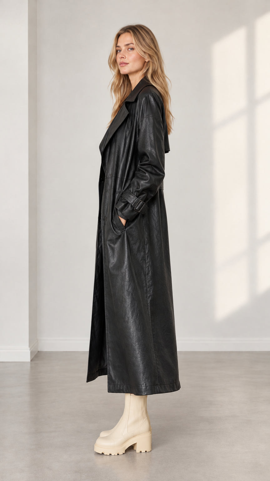 Side profile view of woman modeling long black faux leather trench coat
