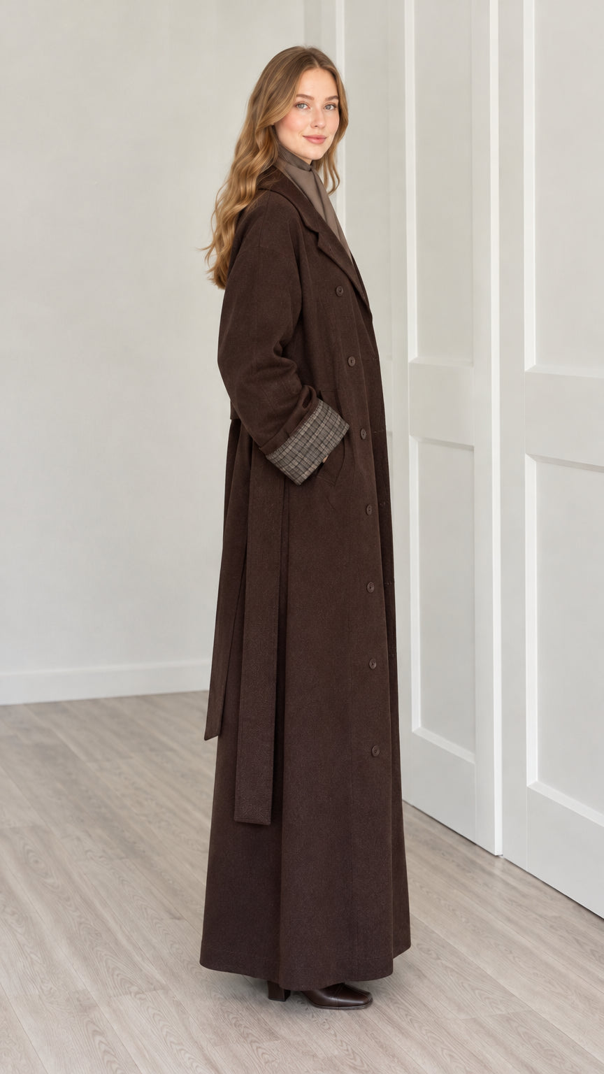Side profile view of woman wearing brown maxi trench coat with tie belt