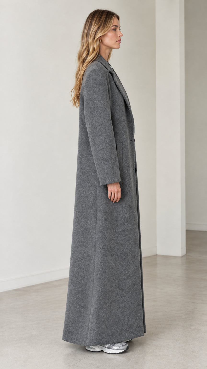 Side profile view of model wearing the long grey maxi coat showing the straight silhouette and floor-skimming hem