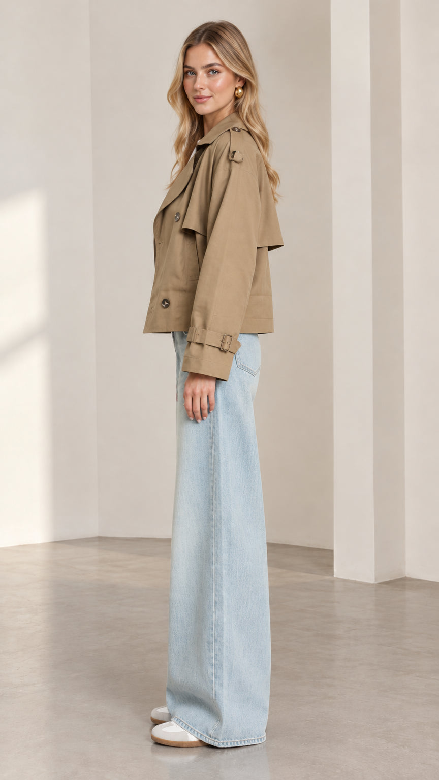 Side profile view of model wearing khaki cropped trench jacket showing tailored sleeve and storm flap