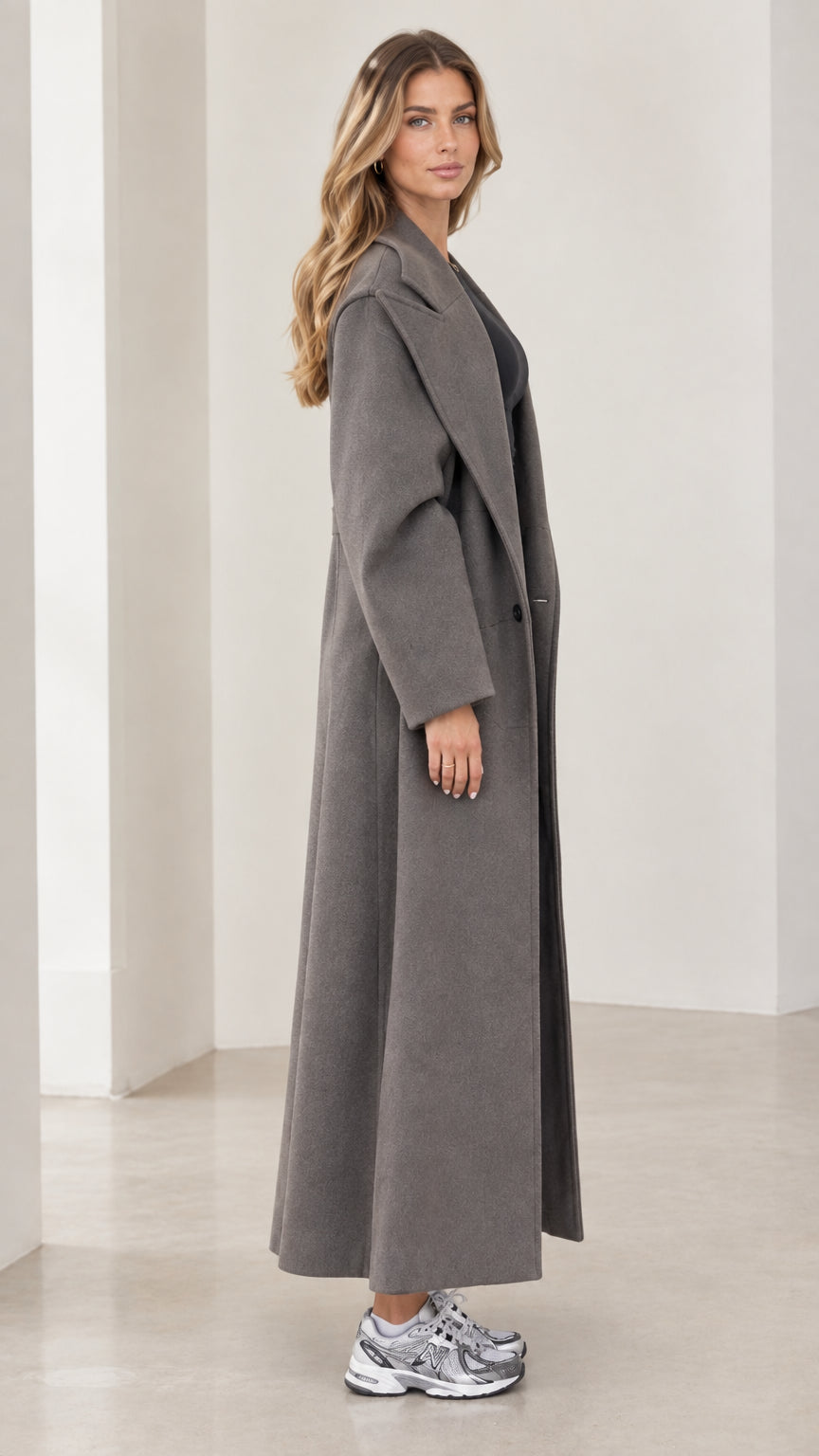 Side profile view of model wearing floor-length charcoal grey tailored overcoat