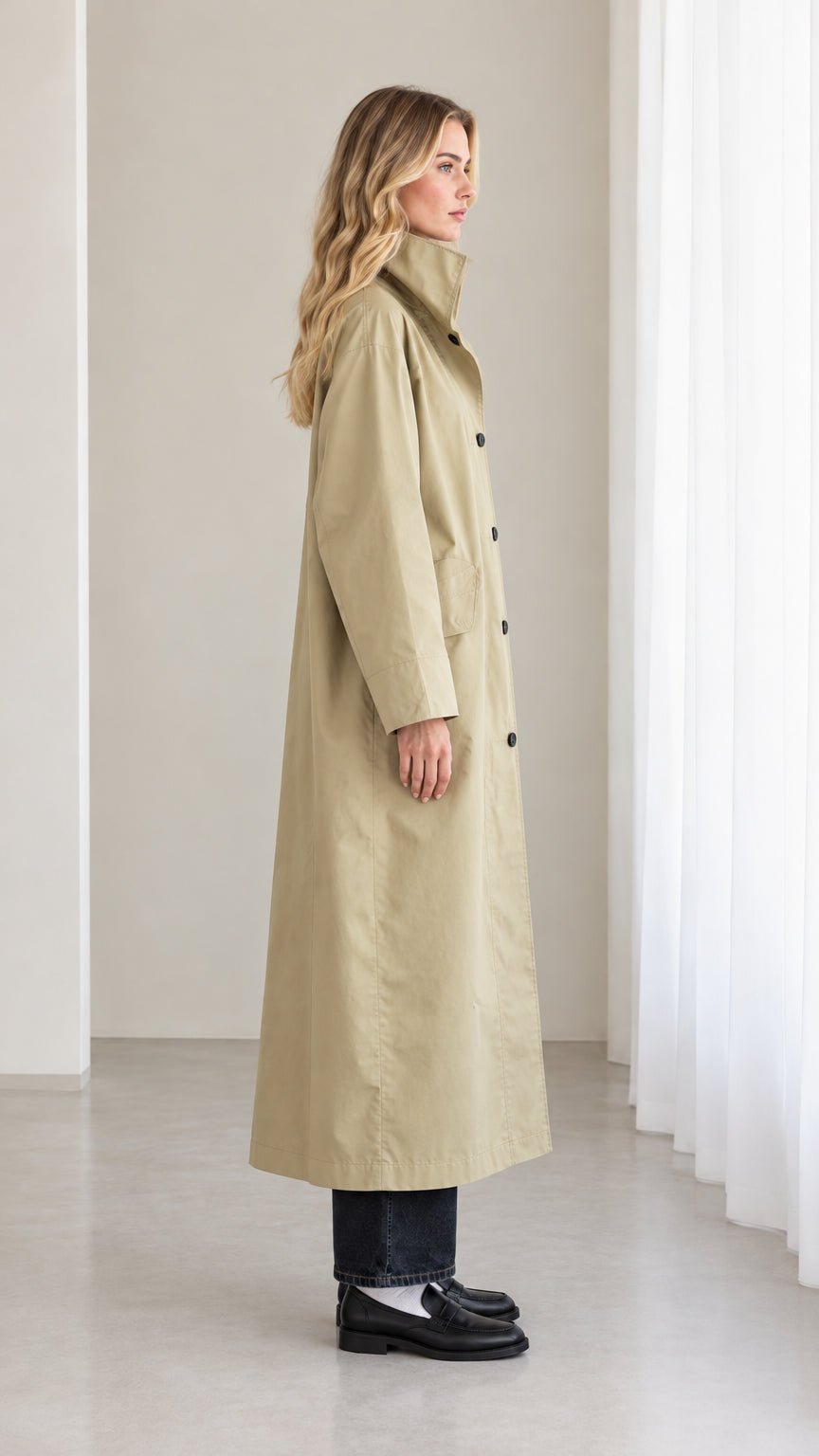 Side profile view of woman wearing sage khaki full-length trench overcoat