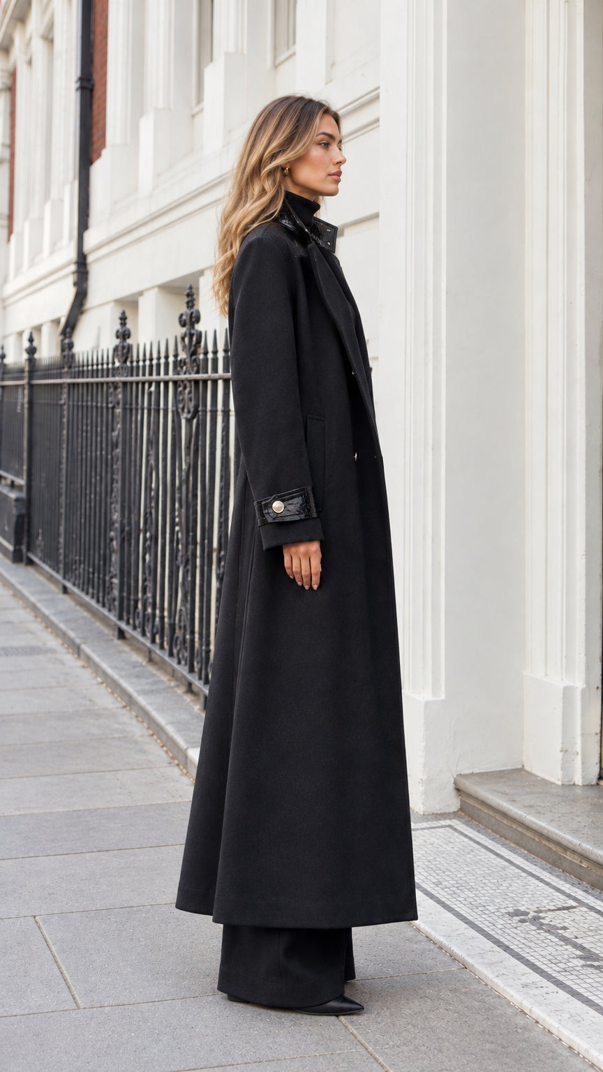Side profile view of woman wearing black maxi tailored overcoat against a classic street backdrop