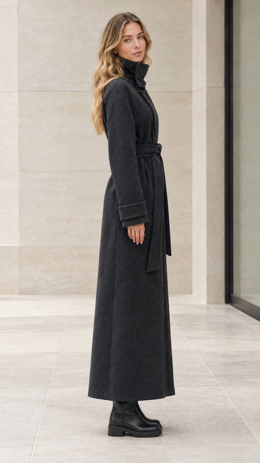 Side profile of woman in full length black belted overcoat showing sleek silhouette