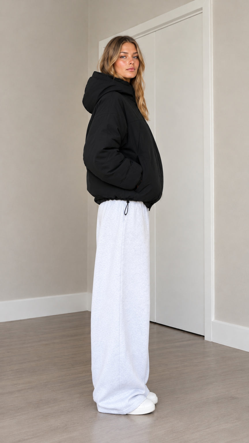 Side profile view of model wearing black hooded puffer jacket showing padded profile