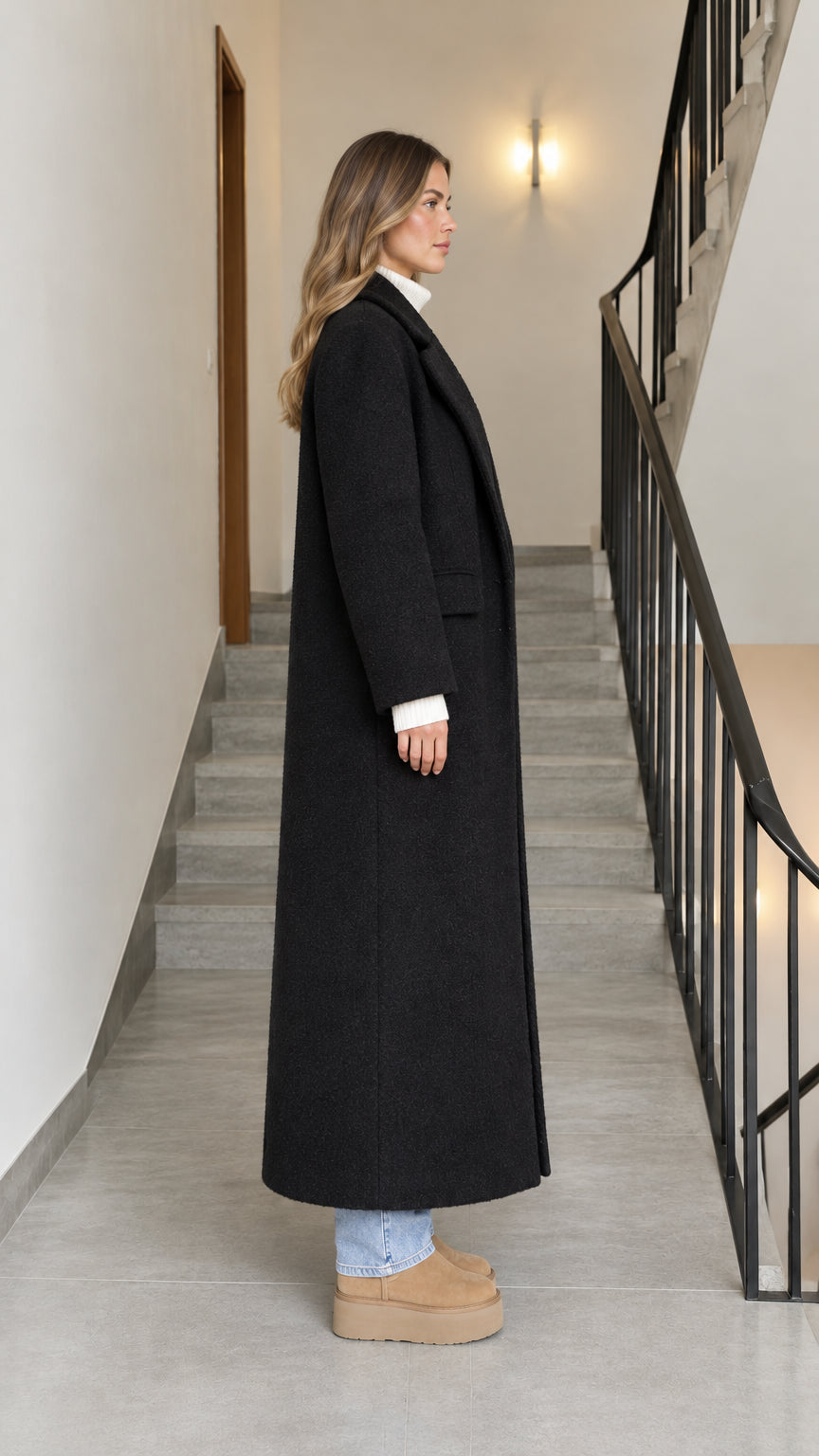 Side profile view of woman wearing a black longline overcoat with flap pocket detail