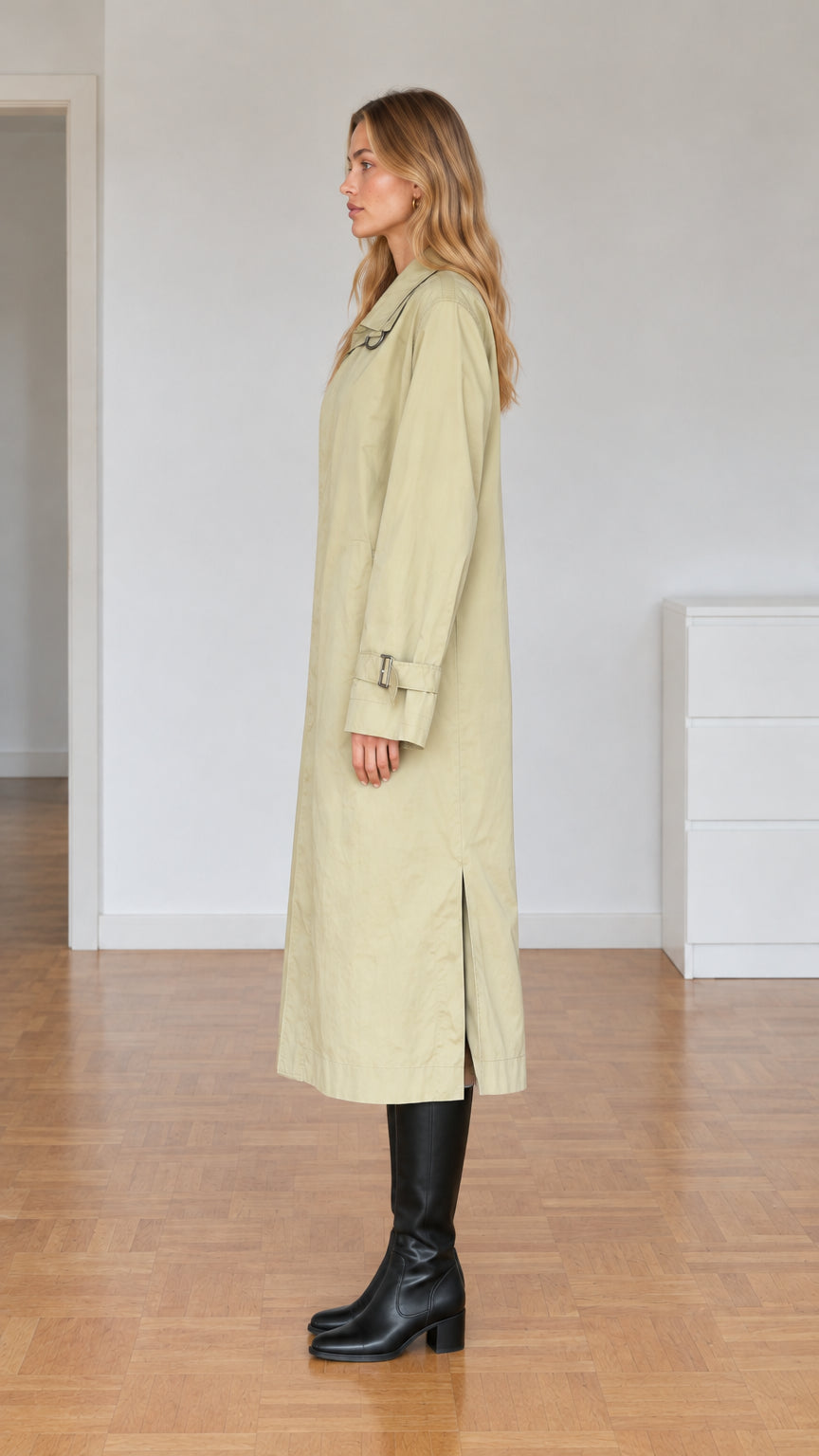 Side profile view of model showcasing full-length sage green trench coat and side slit detail
