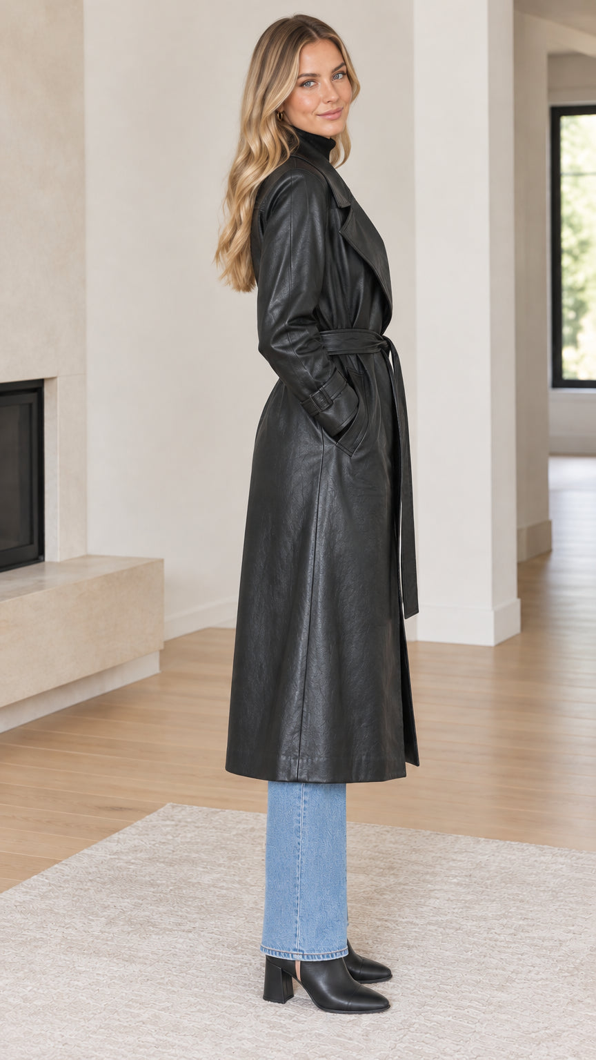 Side profile view of woman modeling long black faux leather trench coat with tie belt