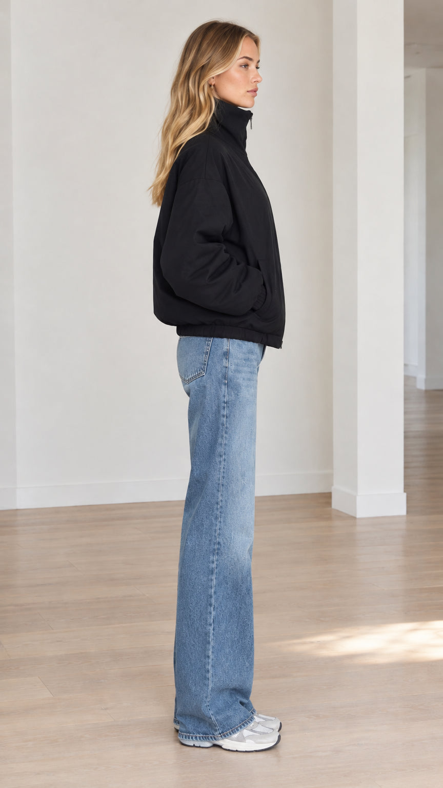 Side profile view of model wearing black zip-up puffer jacket paired with blue jeans