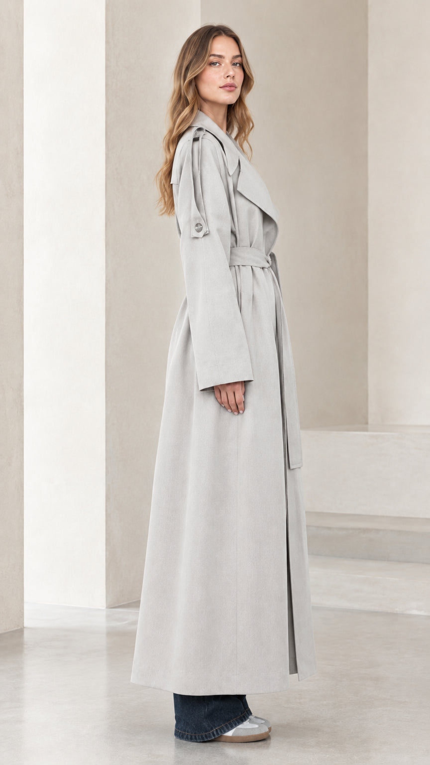 Side profile view of model in full-length light grey trench coat