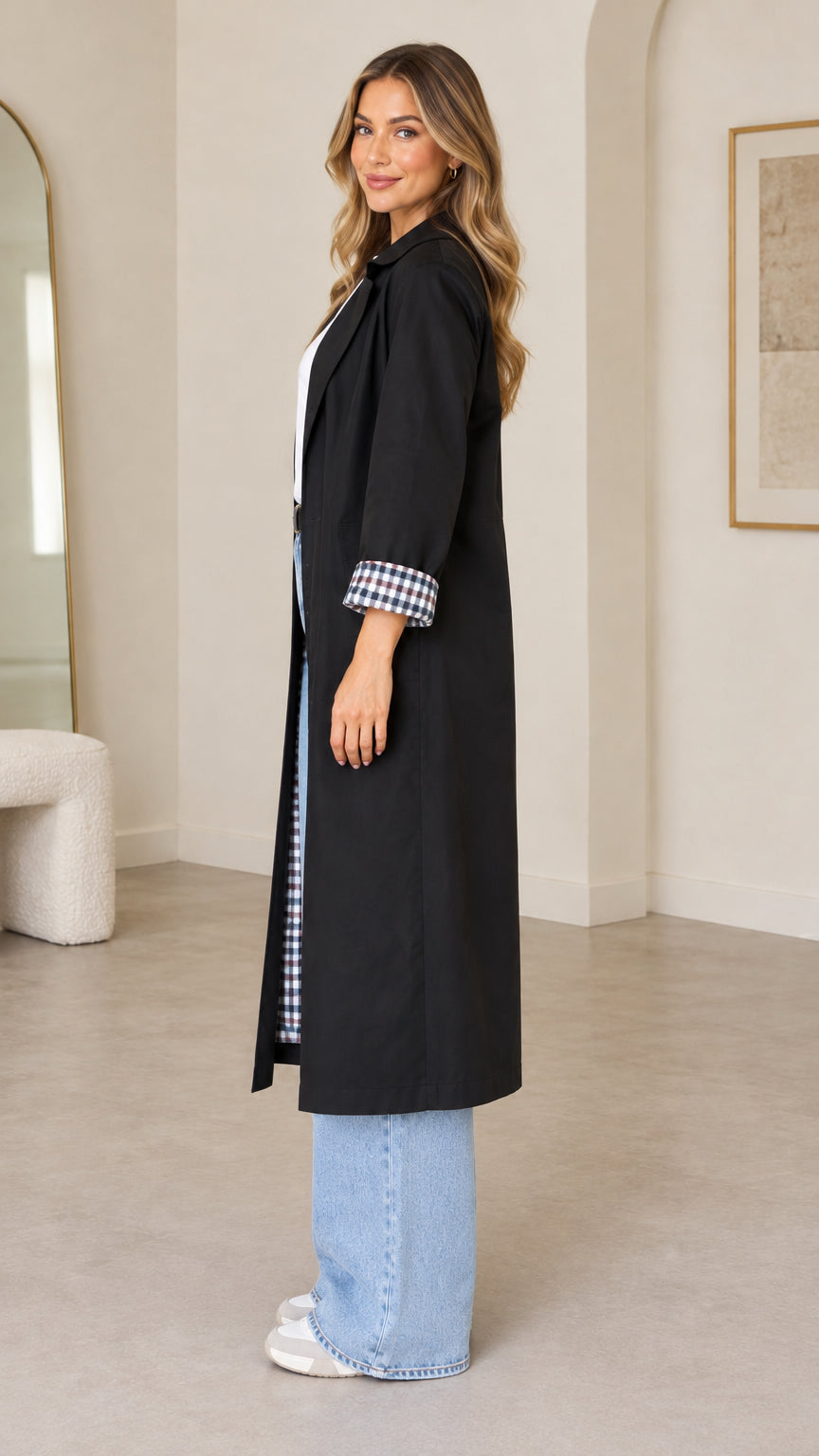 Side full-length view of woman modeling black long duster coat with turn-back plaid cuffs