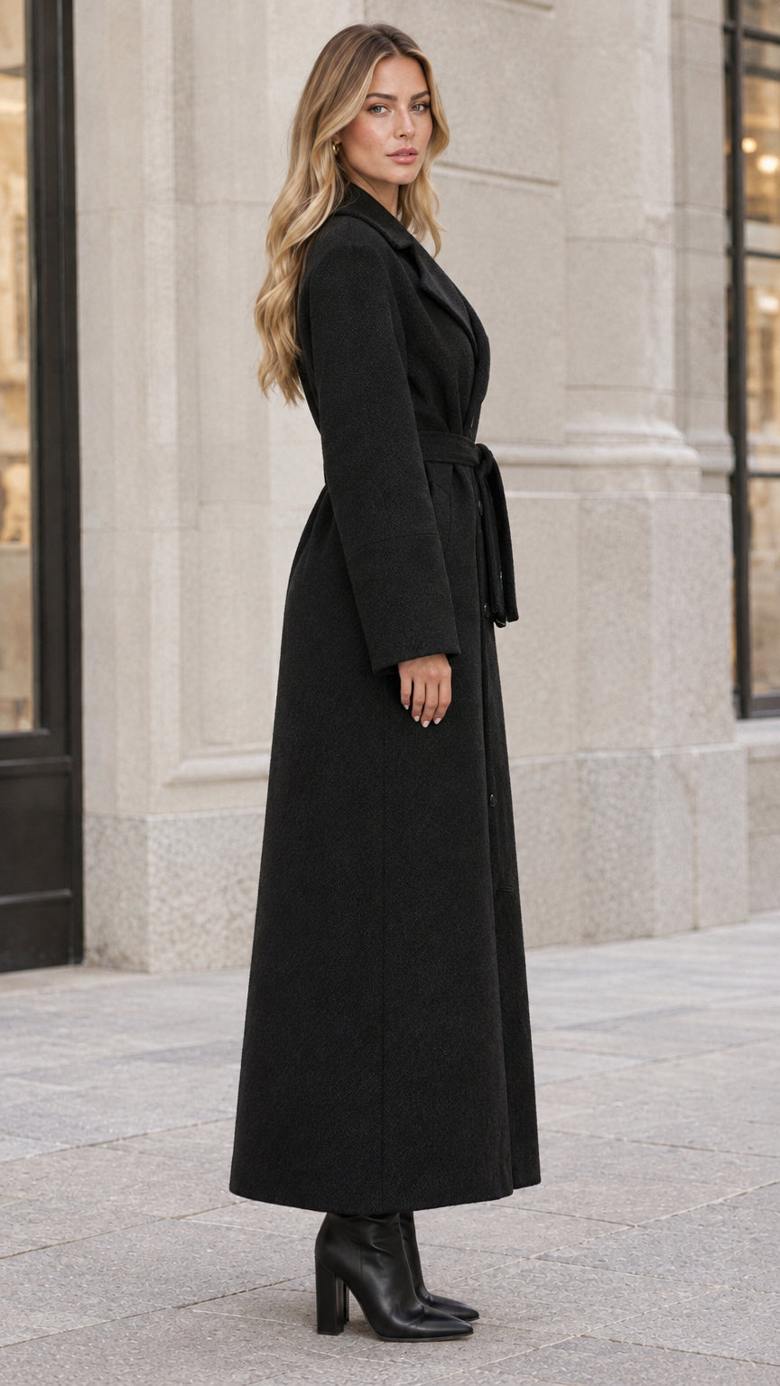 Side profile view of woman wearing an ankle-length black belted overcoat