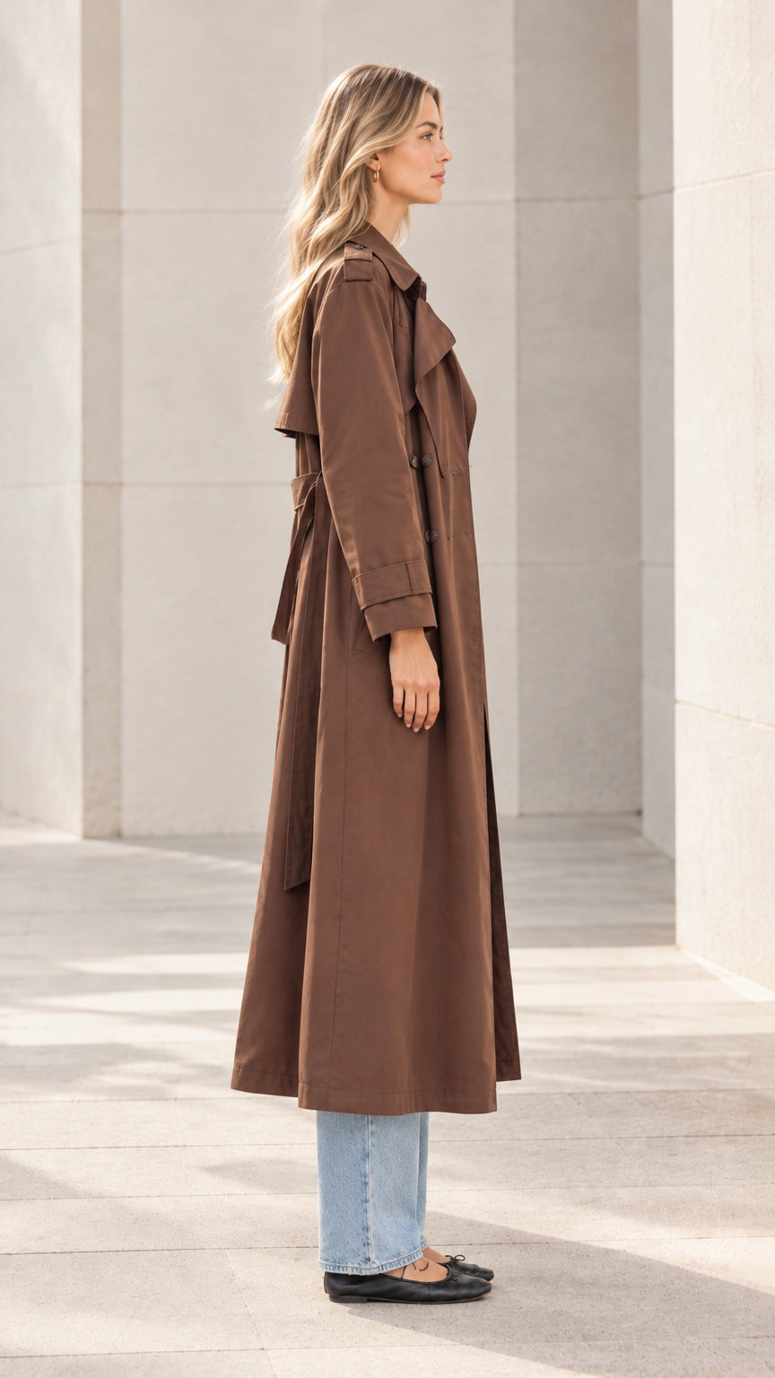 Side profile view of model showcasing the drape and length of the brown trench coat