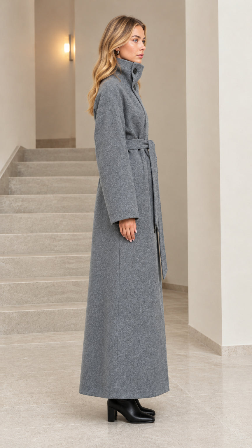 Side profile view of woman wearing grey belted maxi overcoat
