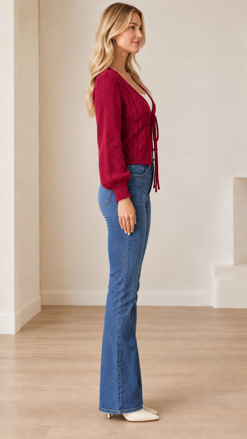 Side profile view of a model in a burgundy tie-front cable knit cardigan with lantern sleeves
