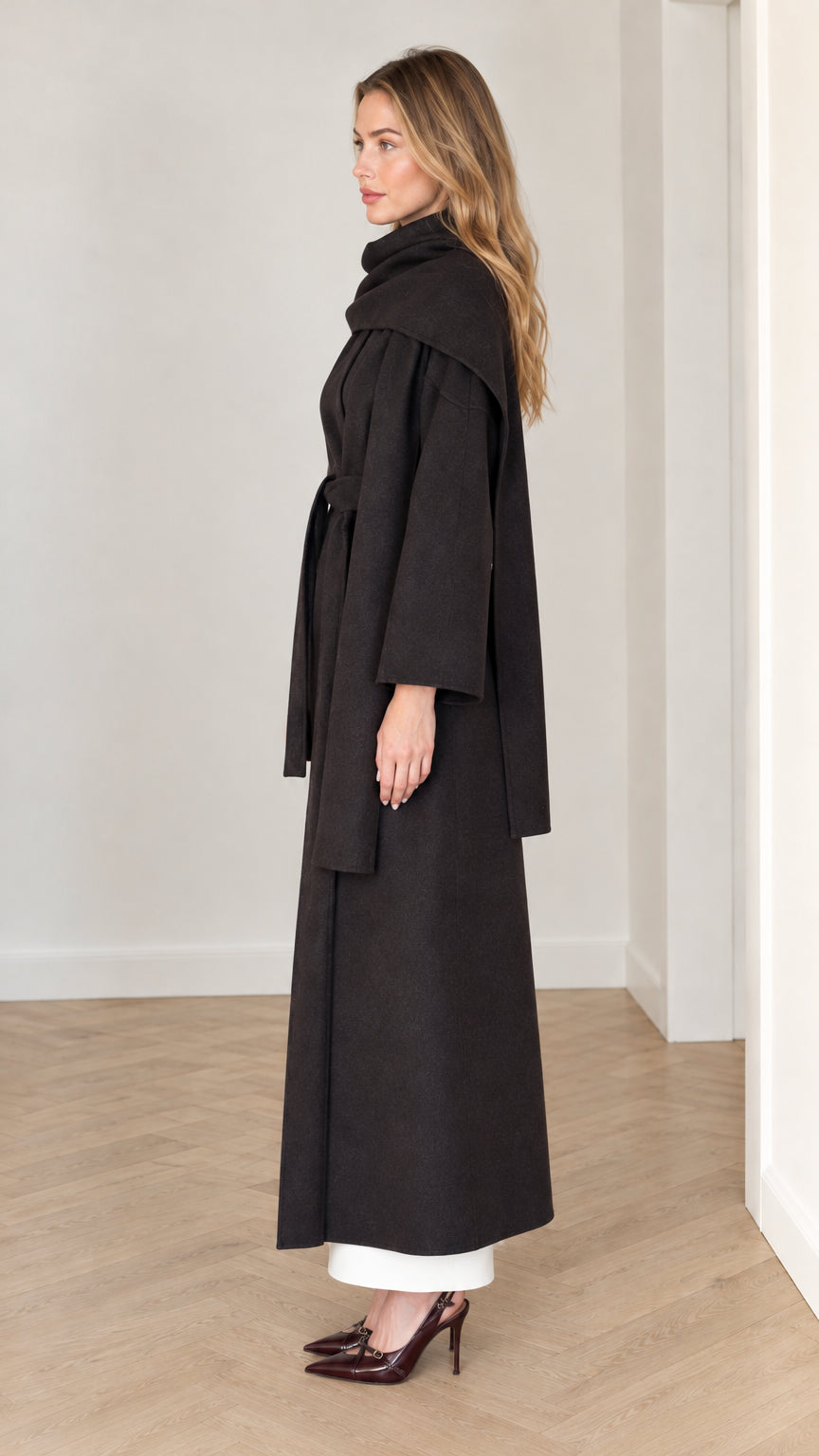 Side view of model wearing black scarf collar maxi coat with tied waist