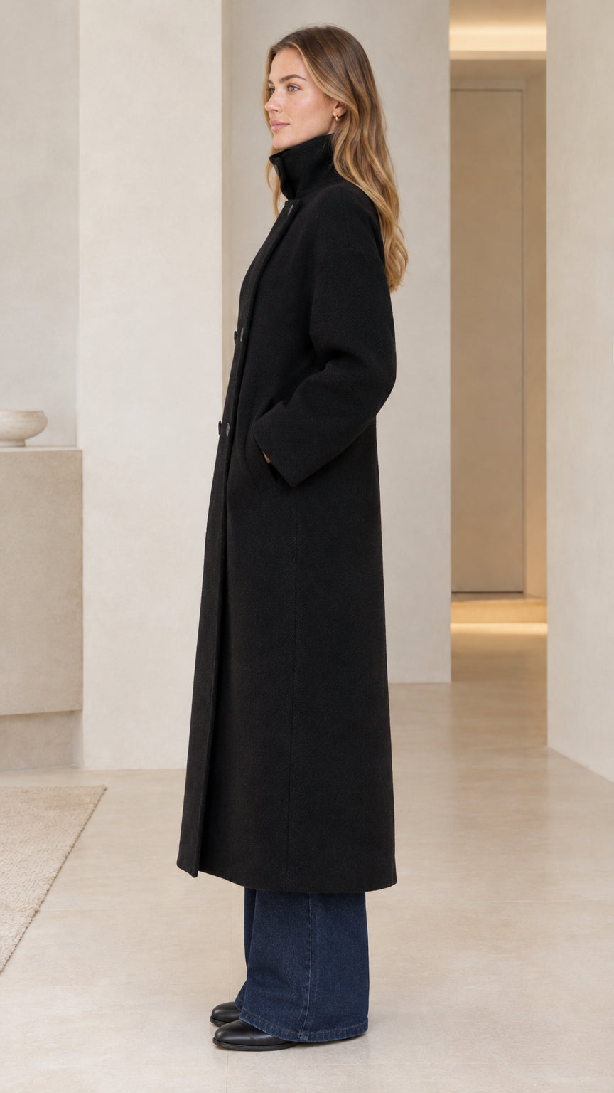 Side angle view of model showcasing full length black tailored longline overcoat