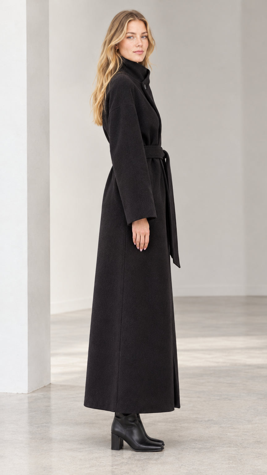 Side profile view of woman wearing full length black belted overcoat
