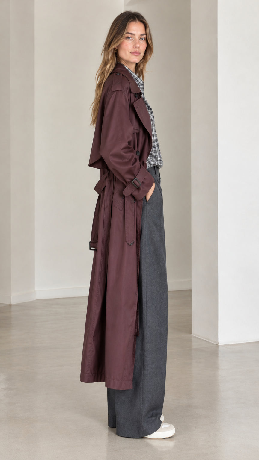 Side profile of model wearing full-length burgundy belted trench coat