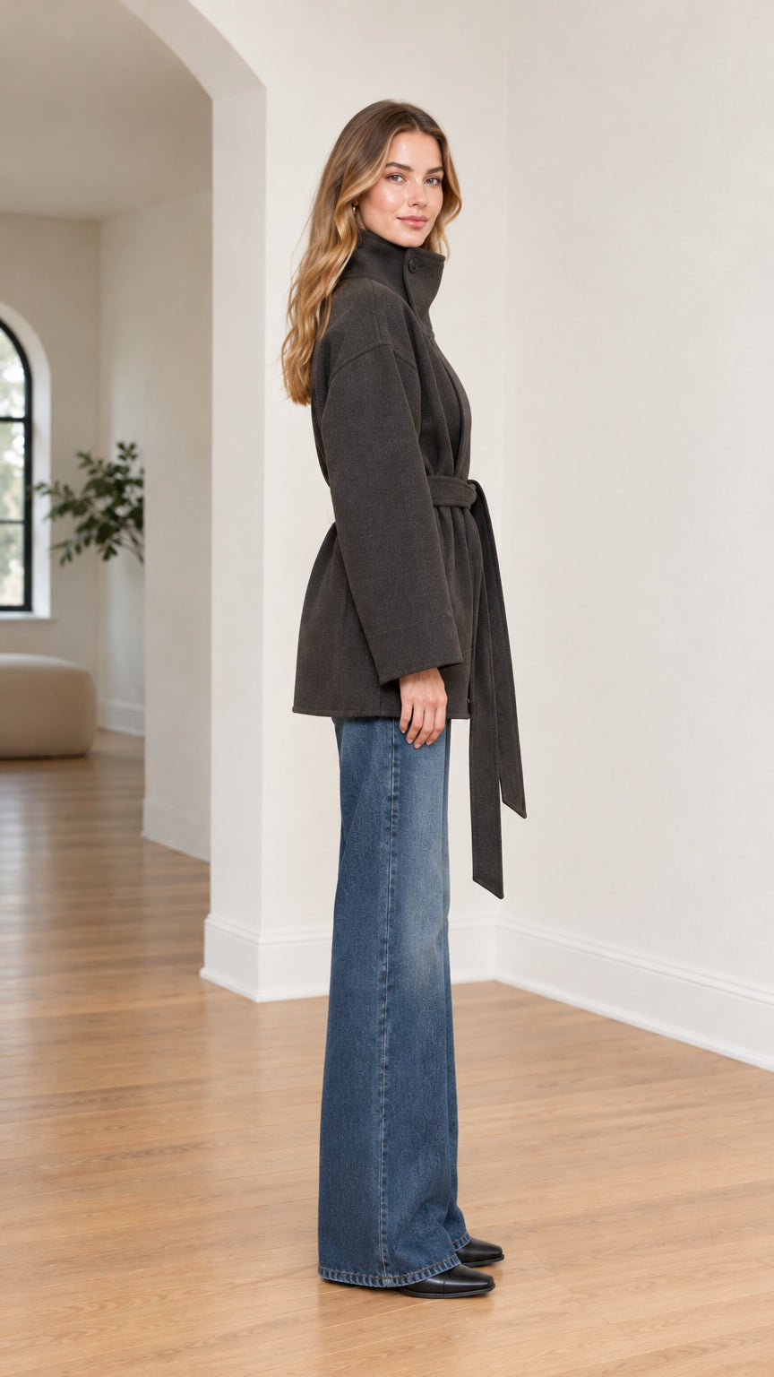 Side profile of model wearing charcoal high-neck wrap coat showing tie belt and stand collar