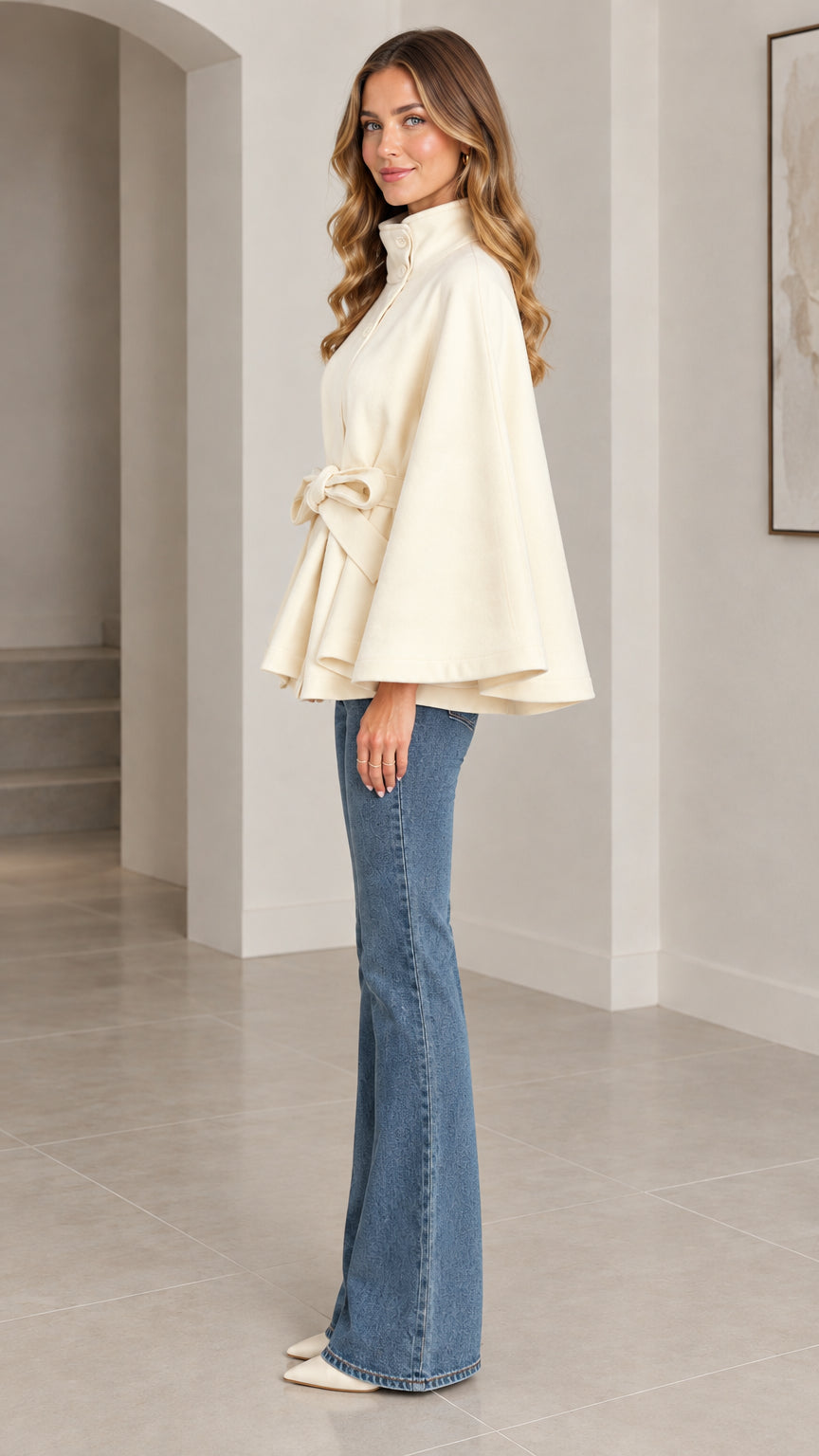 Side profile view of cream belted cape coat highlighting flared silhouette