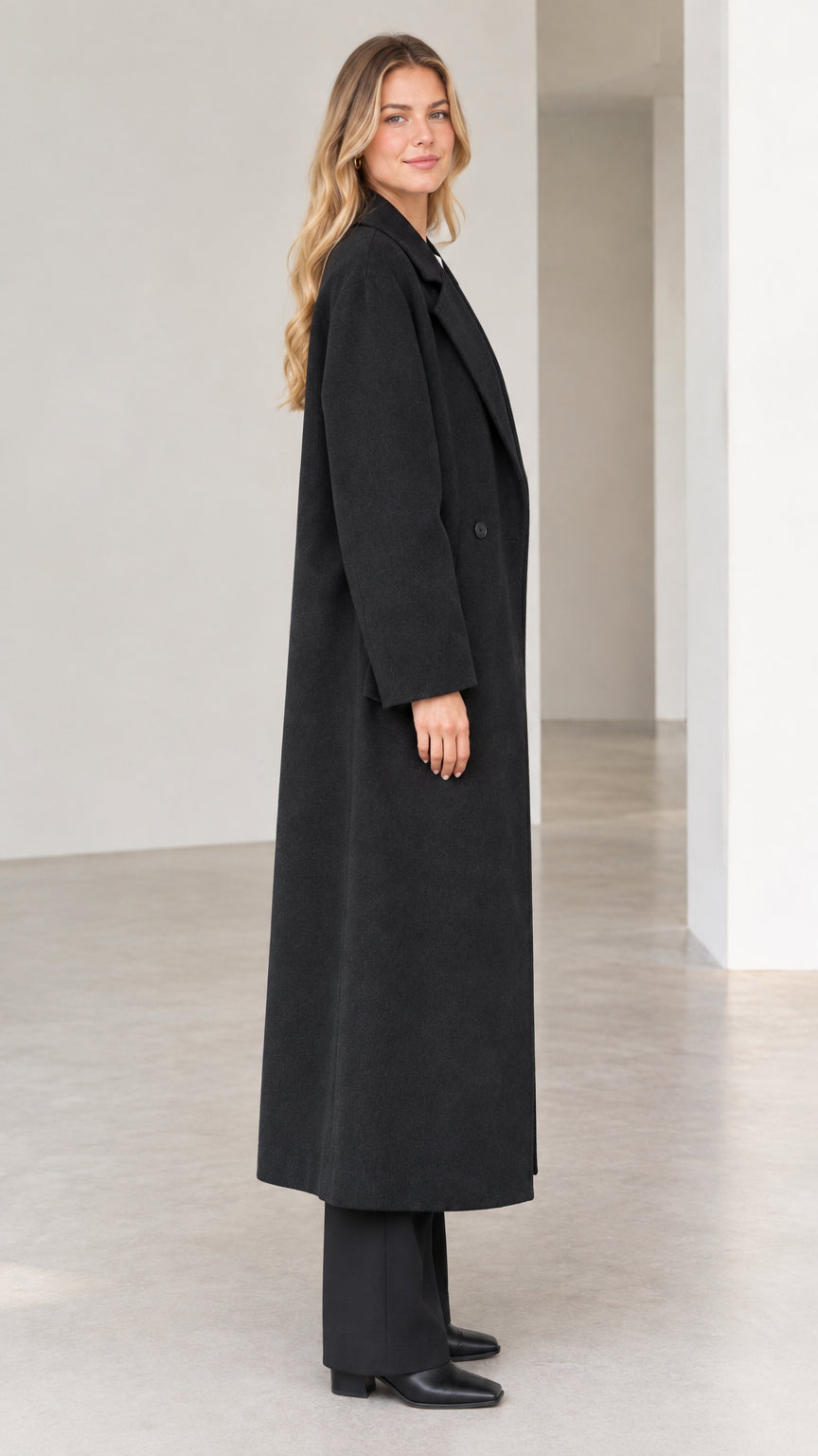Side profile view of woman wearing long black tailored coat