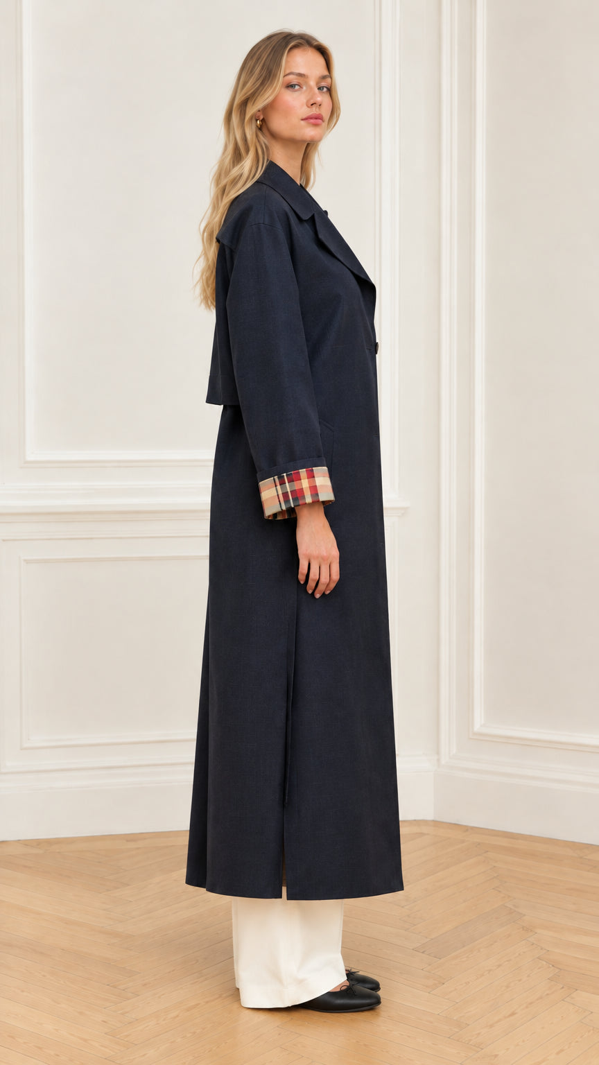 Side profile view of woman wearing navy blue long trench coat with side pleat detail