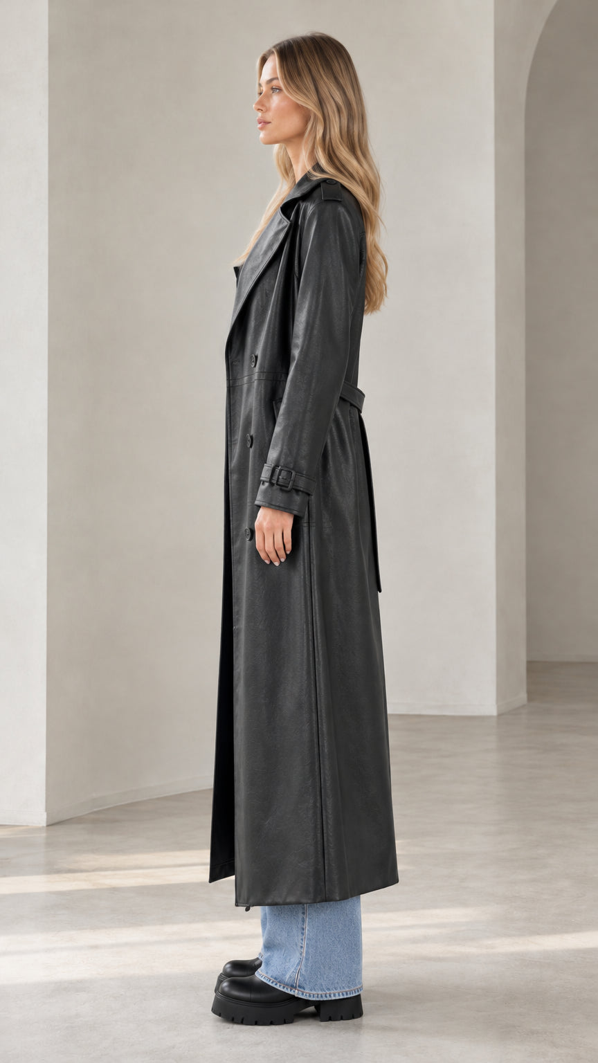 Side profile of model in full-length black faux leather belted trench coat