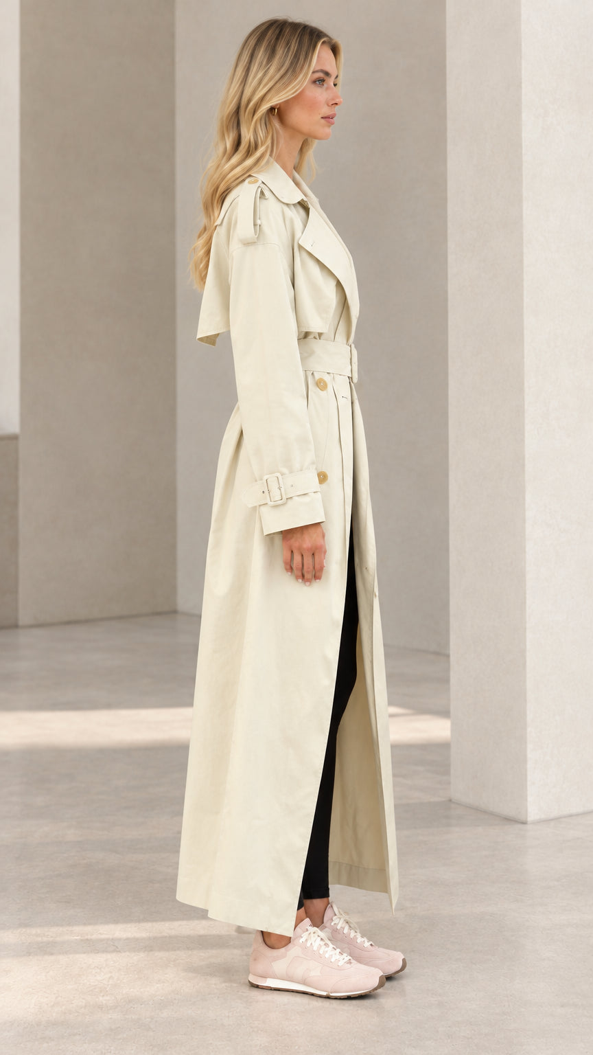 Side profile view of model wearing cream belted maxi trench coat