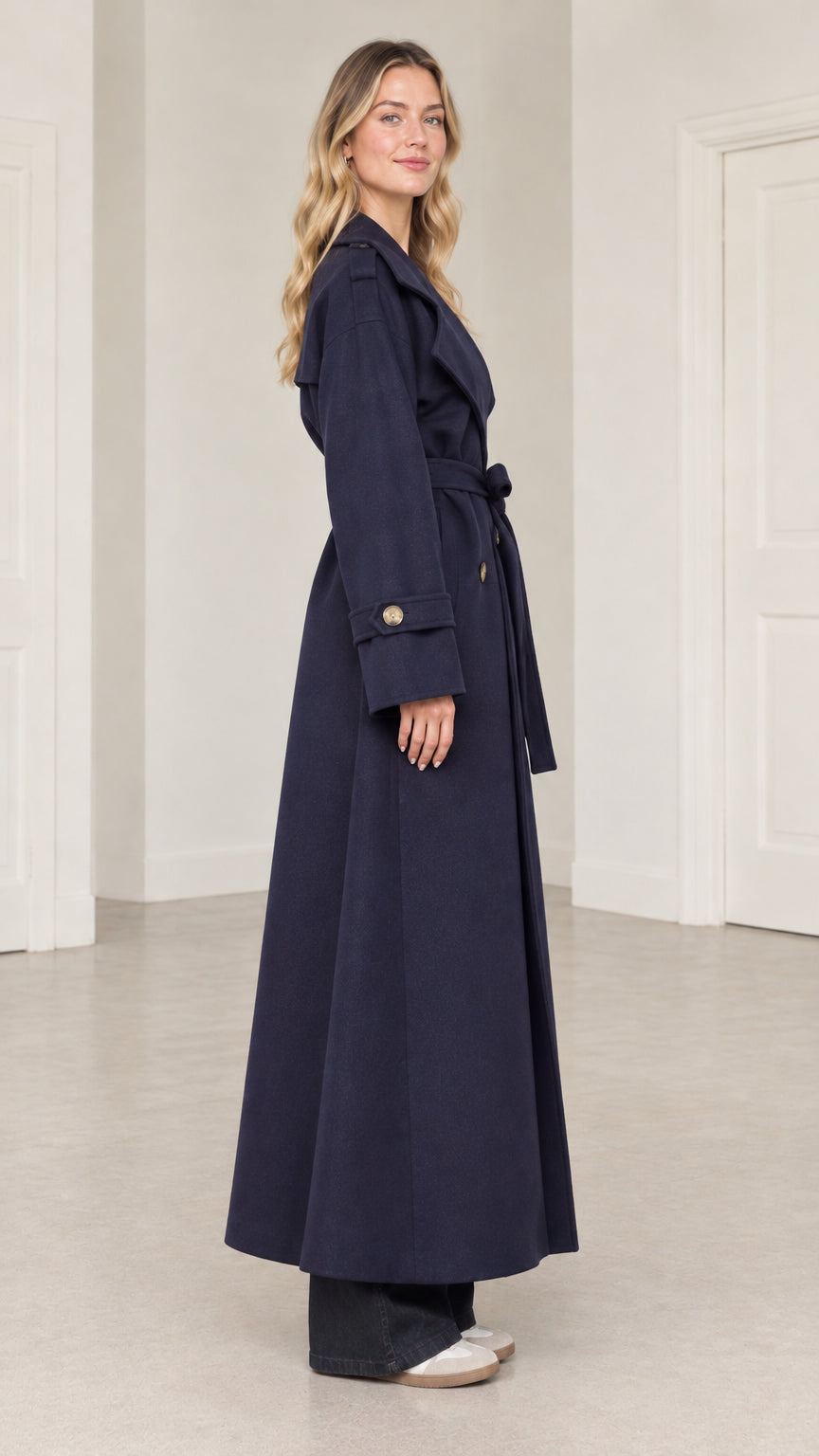 Side profile view of woman wearing navy blue full-length belted overcoat